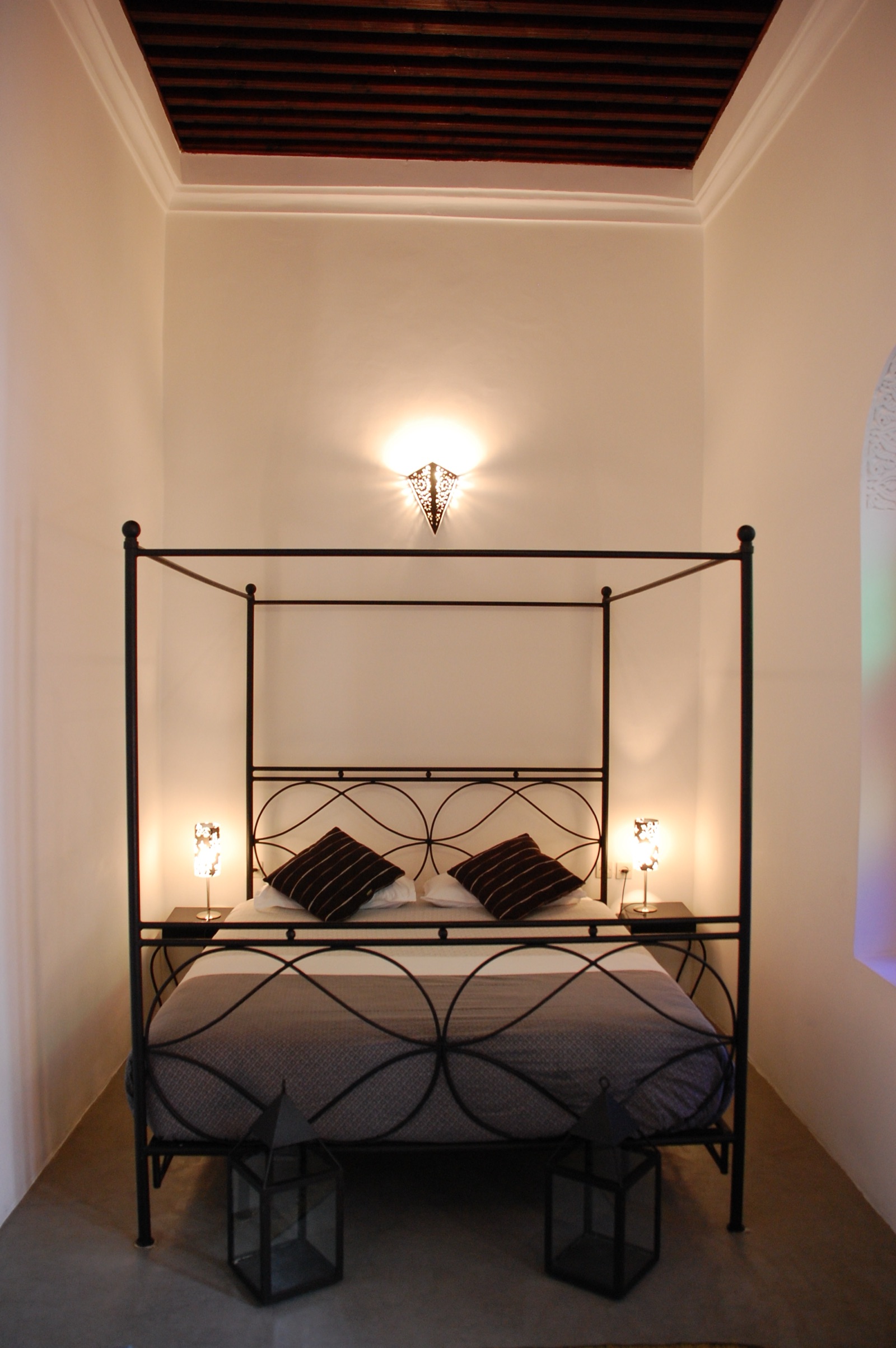 Chambre Hadid : lit à baldaquin en fer forgé, murs blancs et sol en tadelakt gris