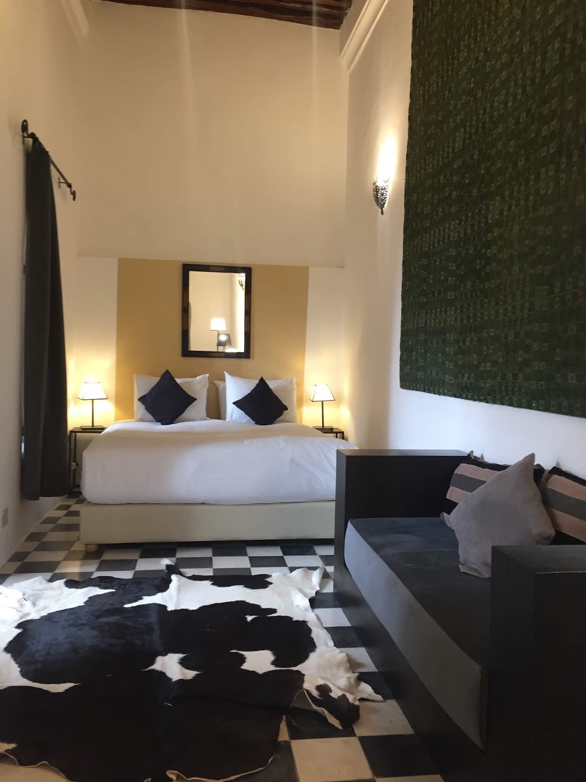 Chambre Soufa : grand lit blanc, banquette sombre, sol en carreaux noirs et blancs et grande tenture verte