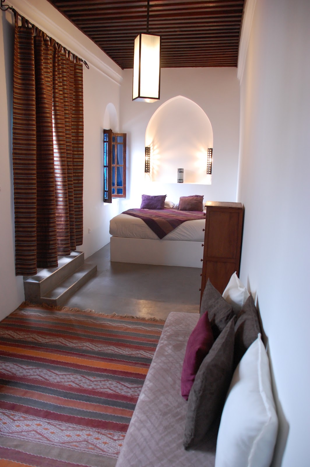 Chambre Terrasse : banquette et tapis berbère au premier plan, lit double sous une niche en arc éclairée