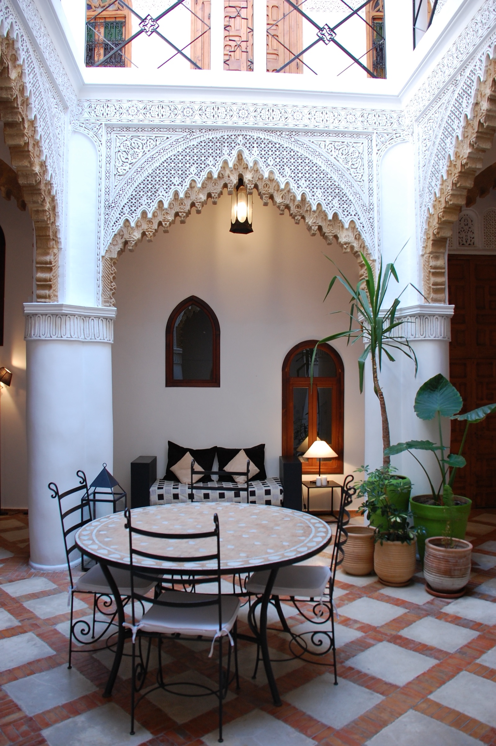Le patio du riad : arcs en plâtre sculpté, table en zellige, plantes et lanterne allumée